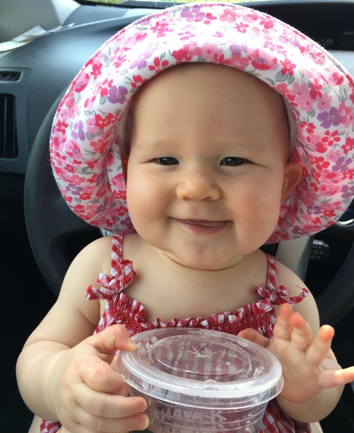 baby in a floral bonnet smiling with big cup of water
